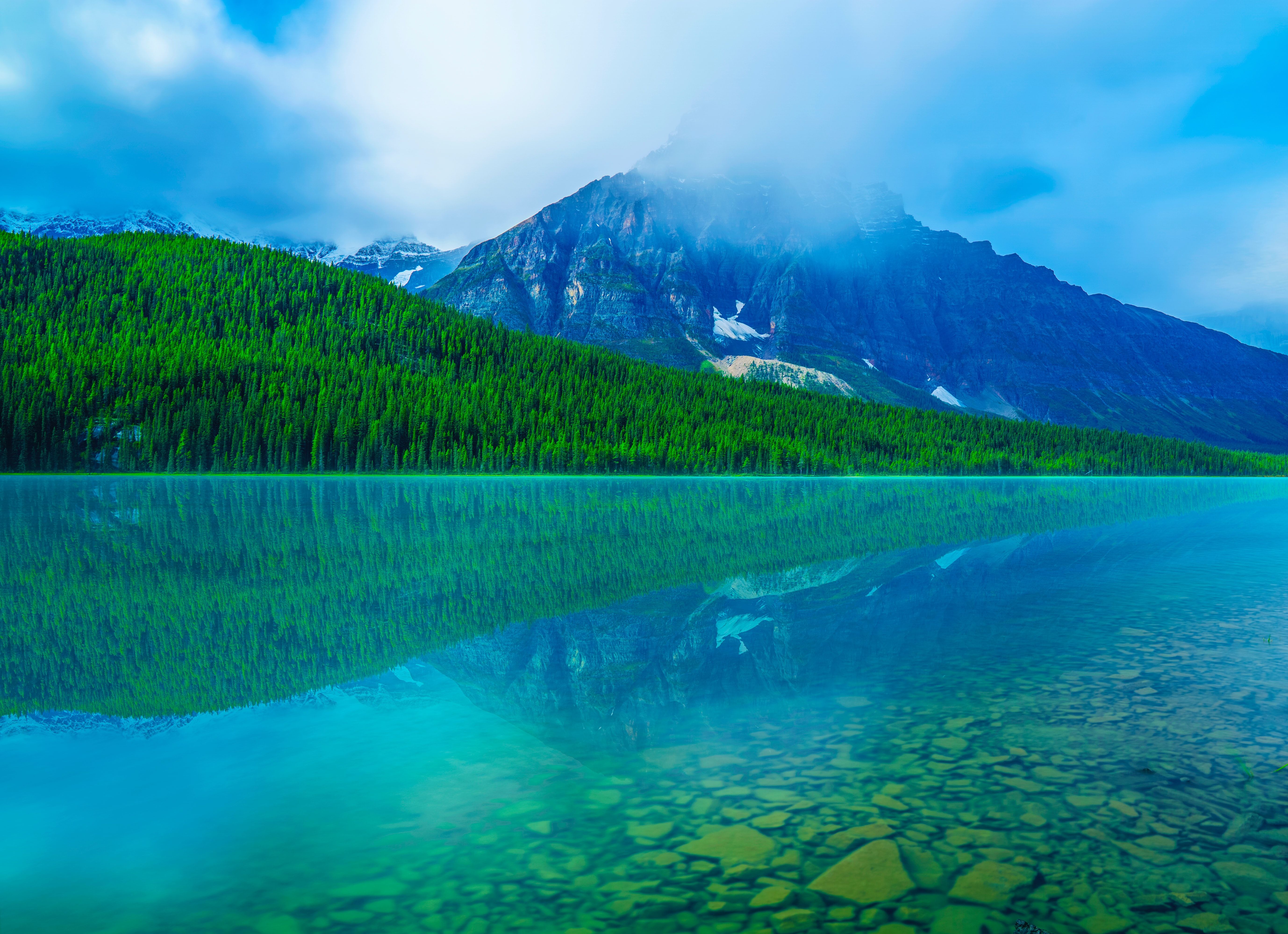 green water reflecting a mountain with clouds